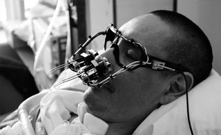 Black & white.'The EyeWriter' A man in a bed with glasses frame and new technology over his nose