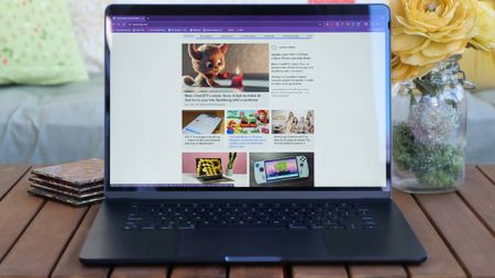 A front-facing view of an open and powered on laptop on top of a wooden table outdoors.