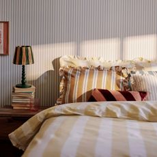 A striped bedroom scheme with mixed stripy bed linen and a green bobbin lamp with a striped shade