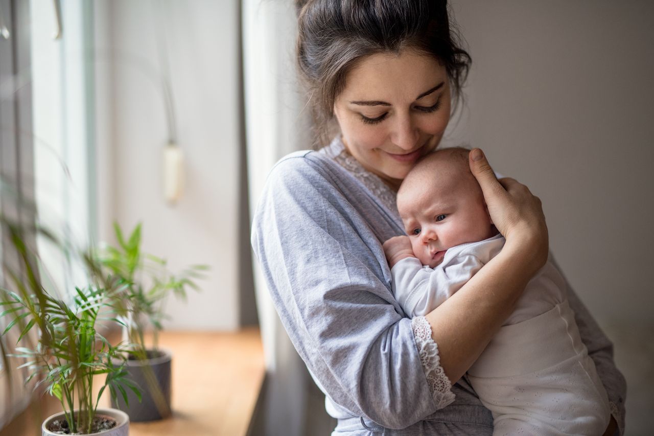 Loving and affectionate mother holding newborn baby indoors at home.