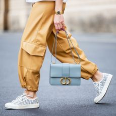 Closeup of the lower half of a woman wearing cargo pants walking while holding a purse.