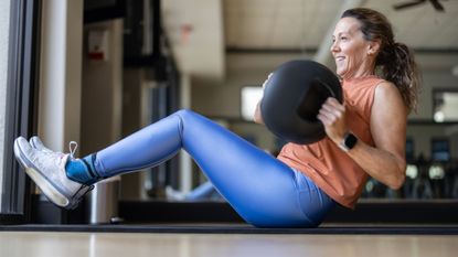 Woman doing Russian twist exercise in the gym with medicine ball sitting on yoga mat