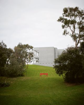 exterior of concrete house on top of hill with red artwork halfway up the hill