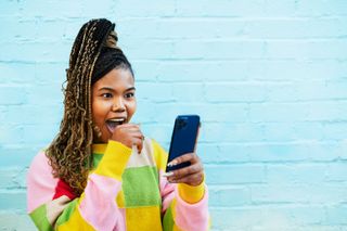 A woman in a colourful jumper looking at her smartphone with a shocked expression