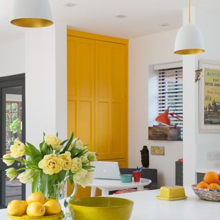 A white kitchen with a yellow-painted door and two pendant lights