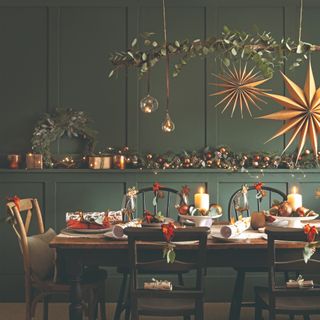 A dining room with table set for Christmas dinner decorated with bows, Christmas crackers and hanging star decorations