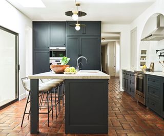 Black kitchen with island and terracotta floor tiles