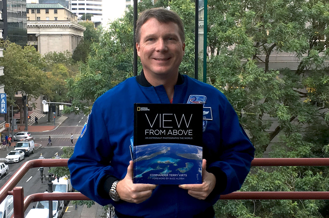 Blue-suited man poses holding a book with the arc of Earth from space on it.