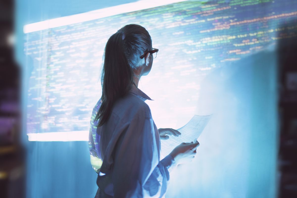 A woman stood in front of a large projector screen with lines of colourful code displayed