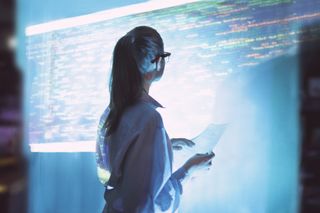 A woman stood in front of a large projector screen with lines of colourful code displayed