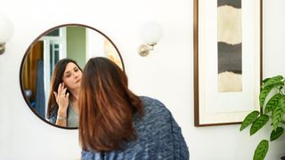 Woman looking in mirror to check hair after asking gynecologist about menopause