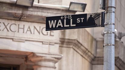 Wall Street street sign with New York Stock Exchange building in background.