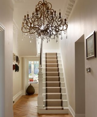 hallway in a victorian home with chandelier, stair runner and herringbone flooring