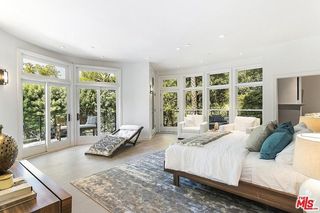 A white bedroom with large windows, a blue-gray area rug, and a wooden bed frame