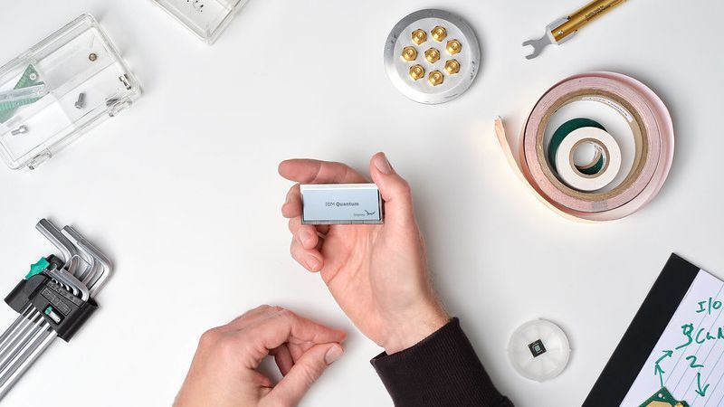 A hand holding the new Osprey quantum processor on a table with equipment