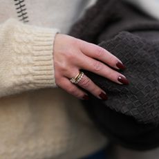 a person with dark red nails wearing a cream sweater and holding a dark brown bag