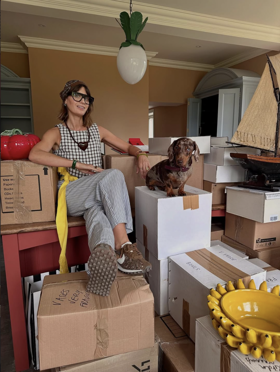 Sarah Corbett-Winder sitting on a pile of packing boxes with her sausage dog