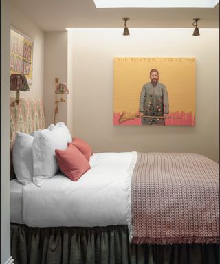 neutral soft pink painted bedroom with a large painting on one wall of a man and a large bed with a patterned headboard and pink and green linens