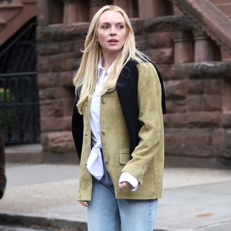 Lindsay wears a suede jacket, white button-down shirt, black sweater, and light-wash jeans.