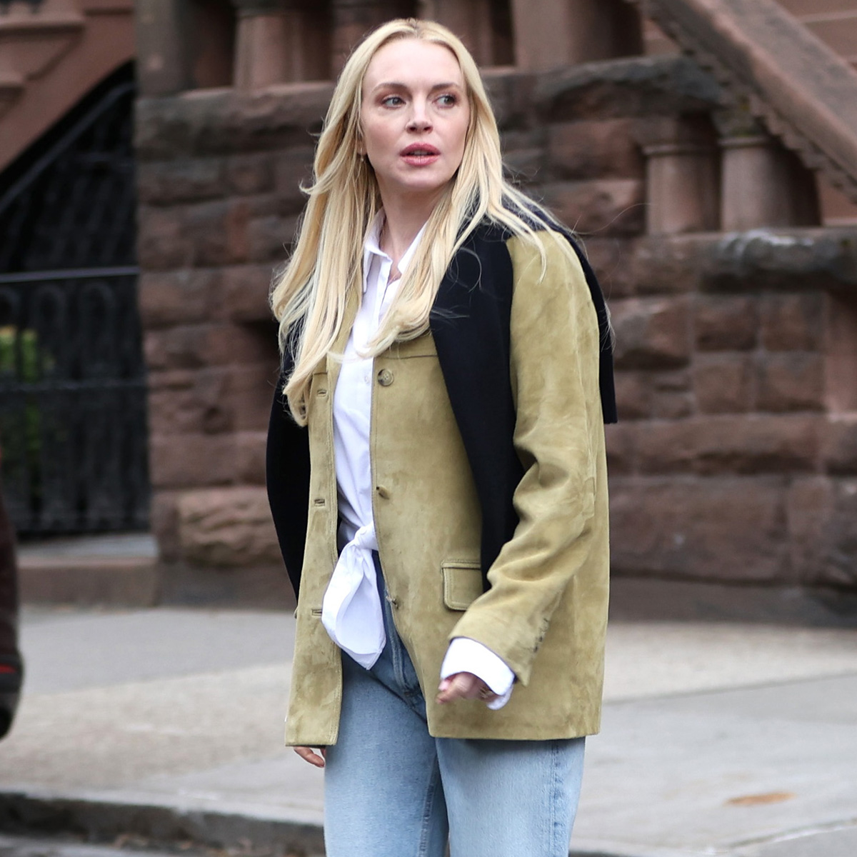 Lindsay wears a suede jacket, white button-down shirt, black sweater, and light-wash jeans.