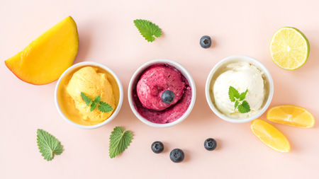 Three types of ice cream surrounded by fruit and berries.