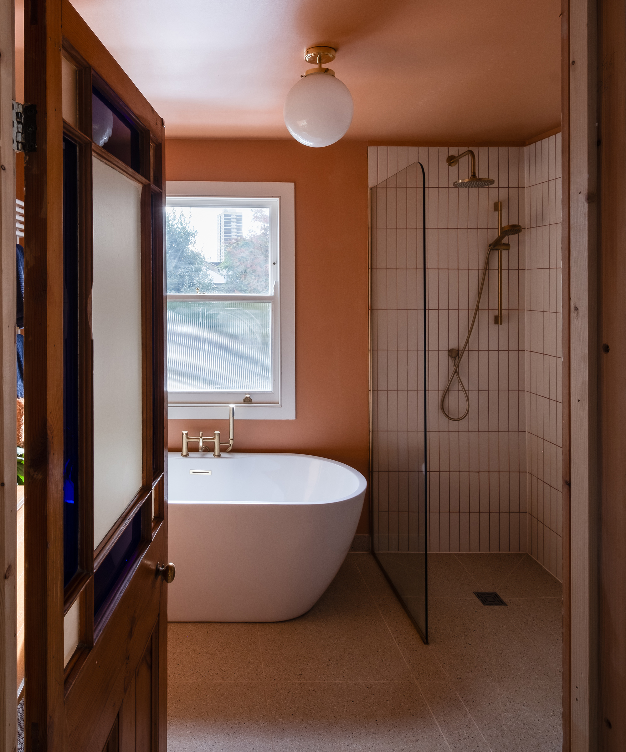 A bathroom with separate walk in shower and freestanding bathtub. The walls are painted a peach colour and there is a globe ceiling light shade