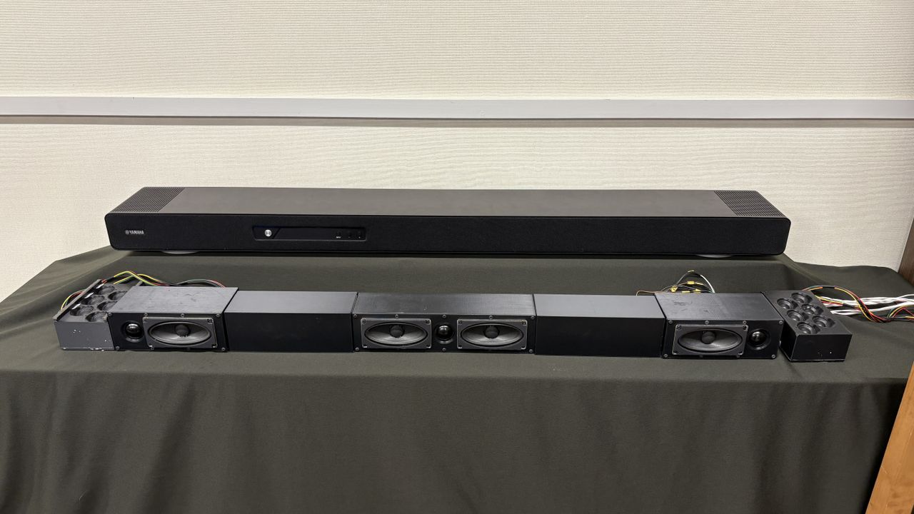 Yamaha True X Surround 90A system (soundbar, surround speakers and subwoofer) in a plain testing room with a TV.
