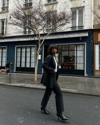 French woman walks down the street wearing black blazer, jeans, boots and white t-shirt