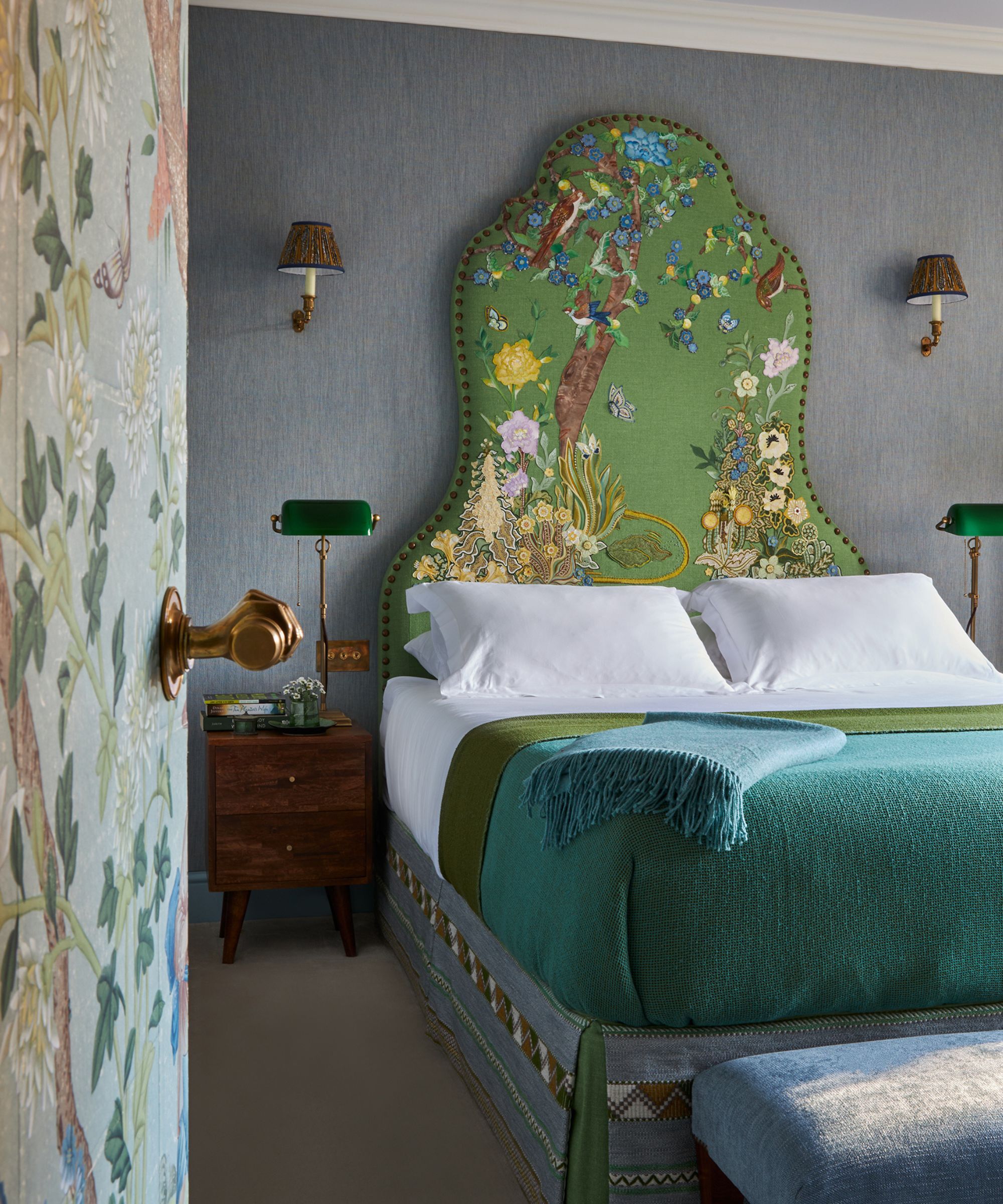 A tall, green headboard with a large embroidered natural scene