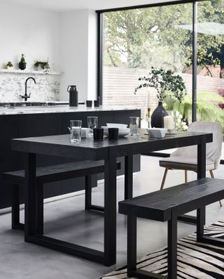 Mono kitchen-diner with architectural table and benches, black island with marble top, and marble backsplash idea.