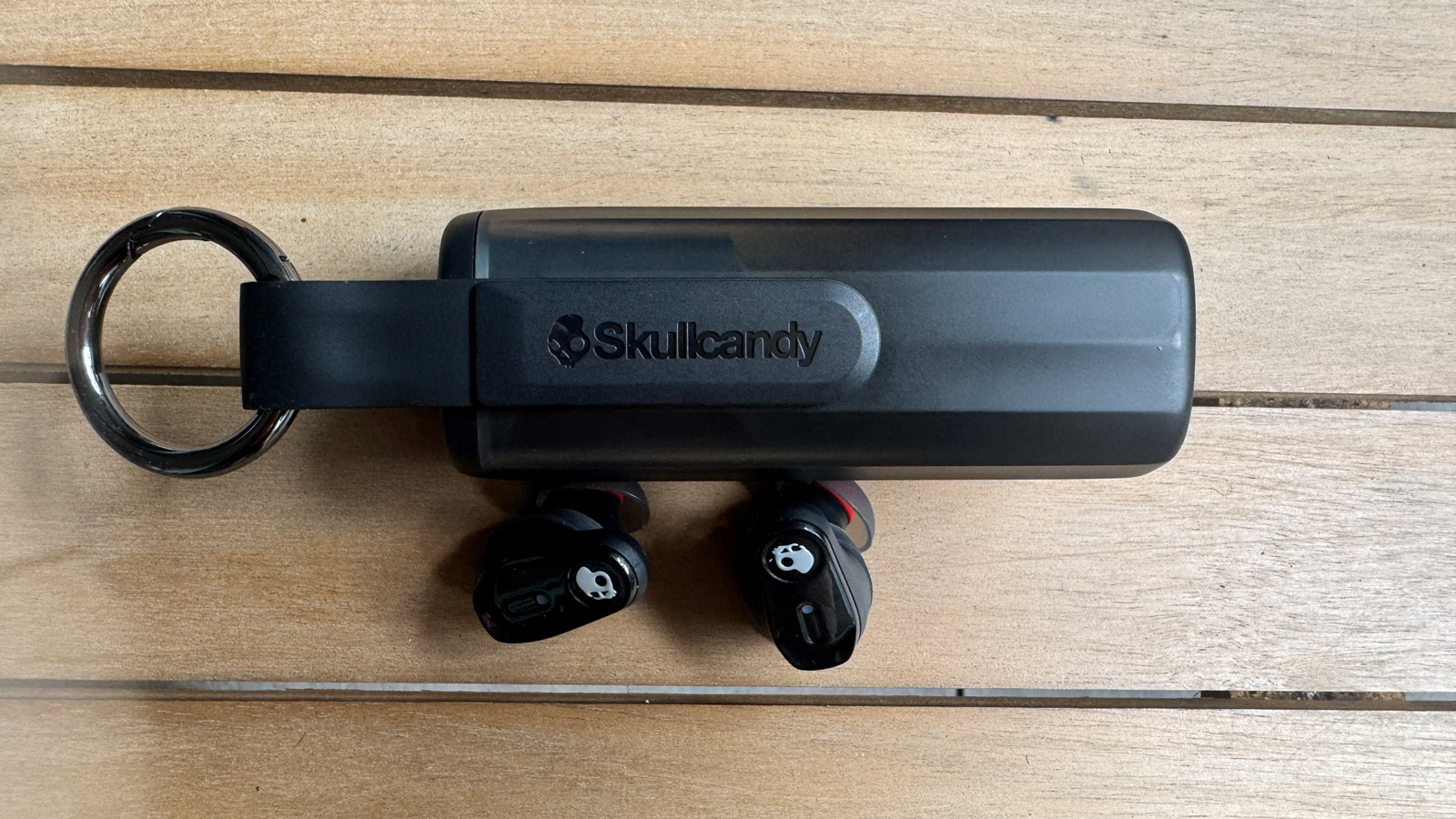 Skullcandy Method 360 ANC earbuds outside their case. The rear of the case shows the Skullcandy logo.
