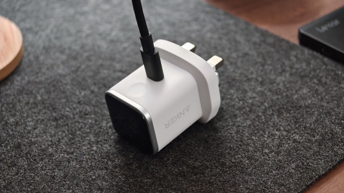 White Anker Nano Charger lying on a dark fabric surface with a USB-C cable connected.