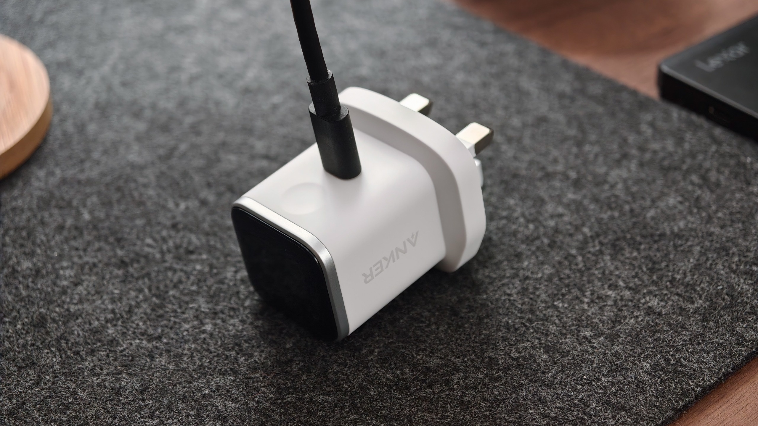 White Anker Nano Charger lying on a dark fabric surface with a USB-C cable connected.