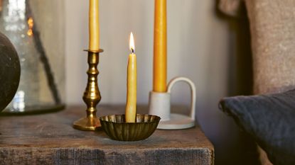 how to make beeswax-dipped candles. Three yellow candles in metal holders on wooden side table