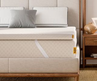 The Nolah Mattress Topper on a bed beside a nightstand.