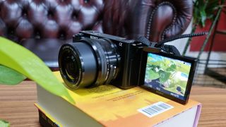 A product shot of the Sony ZV-E10 on a pile of books near a plant