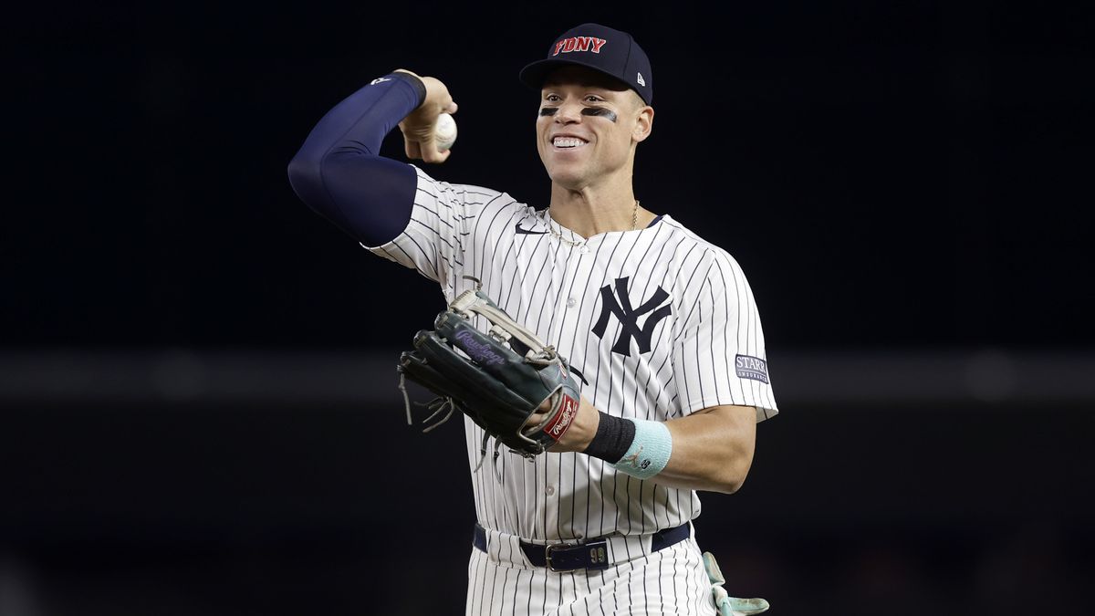 Aaron Judge throws the baseball with a smile in his white and blue pin-striped Yankees uniform.