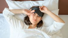 A woman lying on her back wearing an eye mask wakes up after a bad night's sleep on an unsupportive mattress