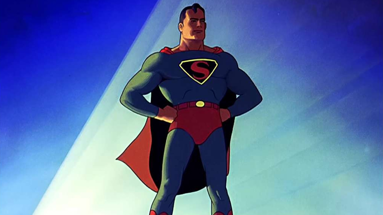 Superman del cómic.  Hombre vestido con un body azul con una S gigante en el pecho.  También lleva pantalones rojos y una capa roja.  Tenía las manos en las caderas en una pose poderosa y segura.