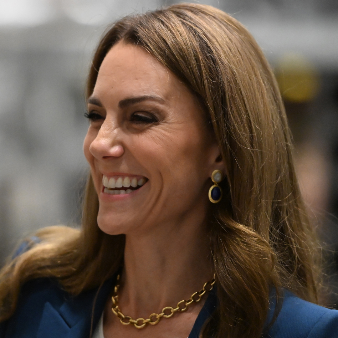 Kate Middleton wearing a blue suit and gold necklace while laughing