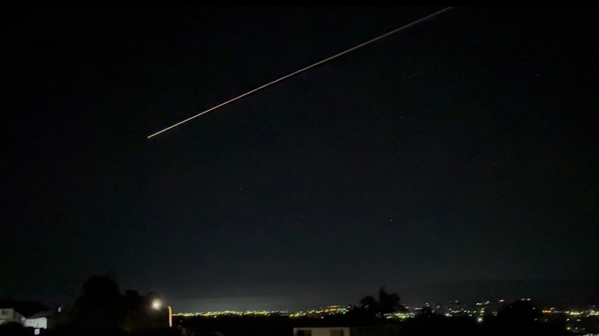 A streak of glowing light is seen in a black night sky above a city