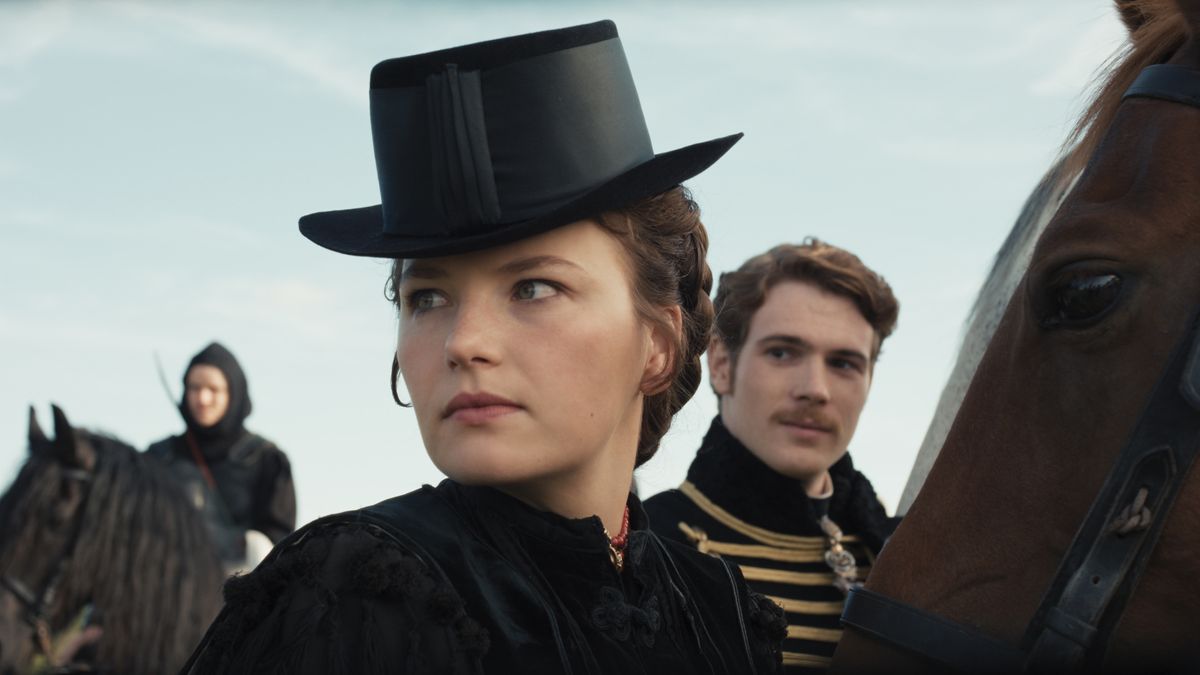 Empress Elisabeth wearing a black hat as Emperor Franz looks at her from behind in The Empress season 2.