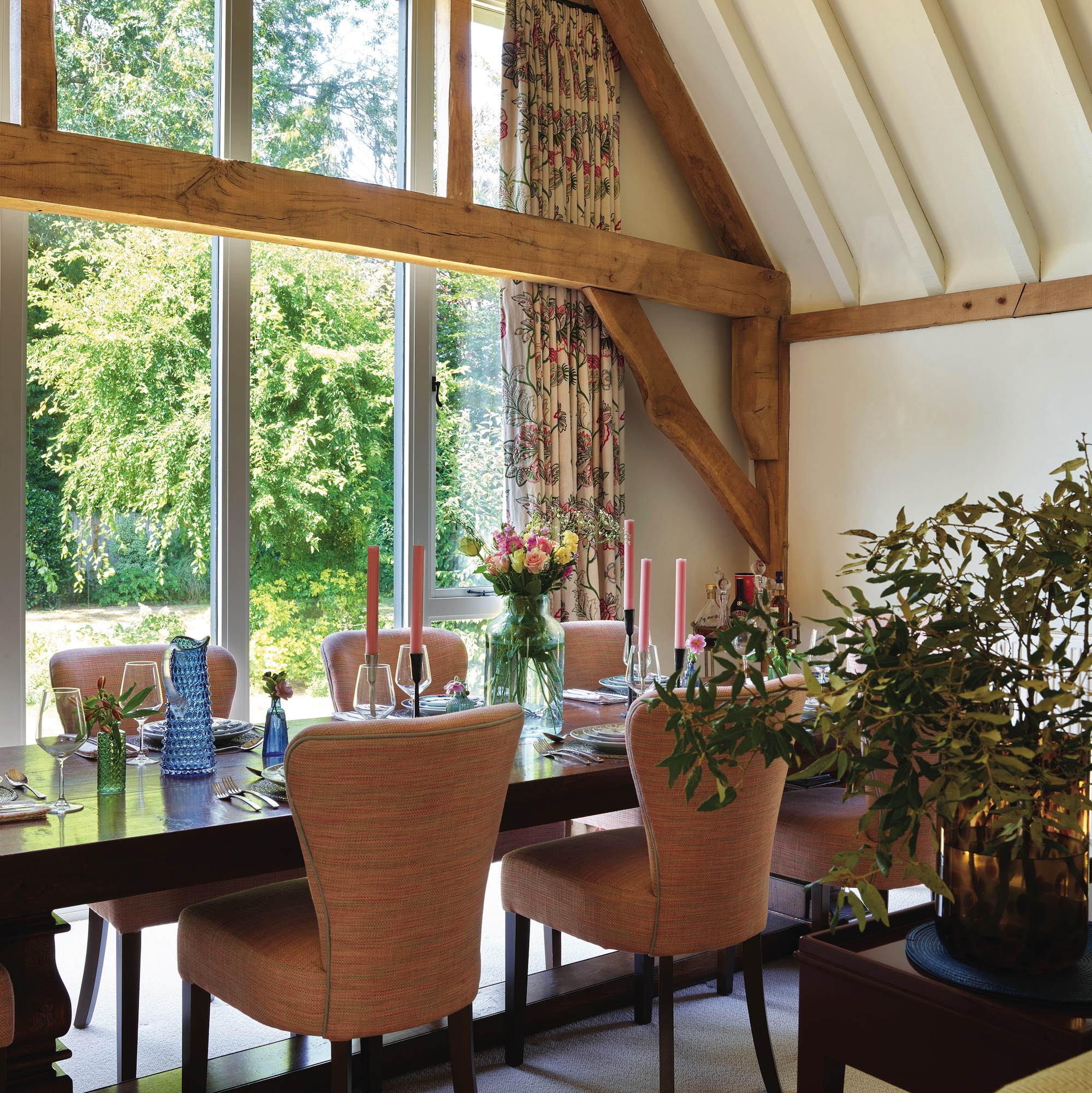 dining table and upholstered chairs in a barn conversion with large windows and vaulted beamed roof