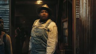 Omar Benson Miller in a hat and overalls boasting a concerned stare into the distance in Sinners