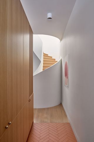 white hallway with oak wall cupboards on one side and curved staircase in front