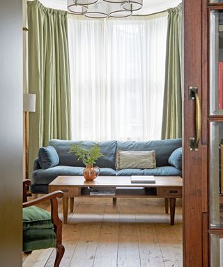 living room with blue sofa, green curtains, wooden flooring and mid century coffee table