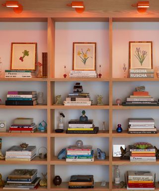 Three vertical wooden bookshelves with books, artwork, and characterful trinkets