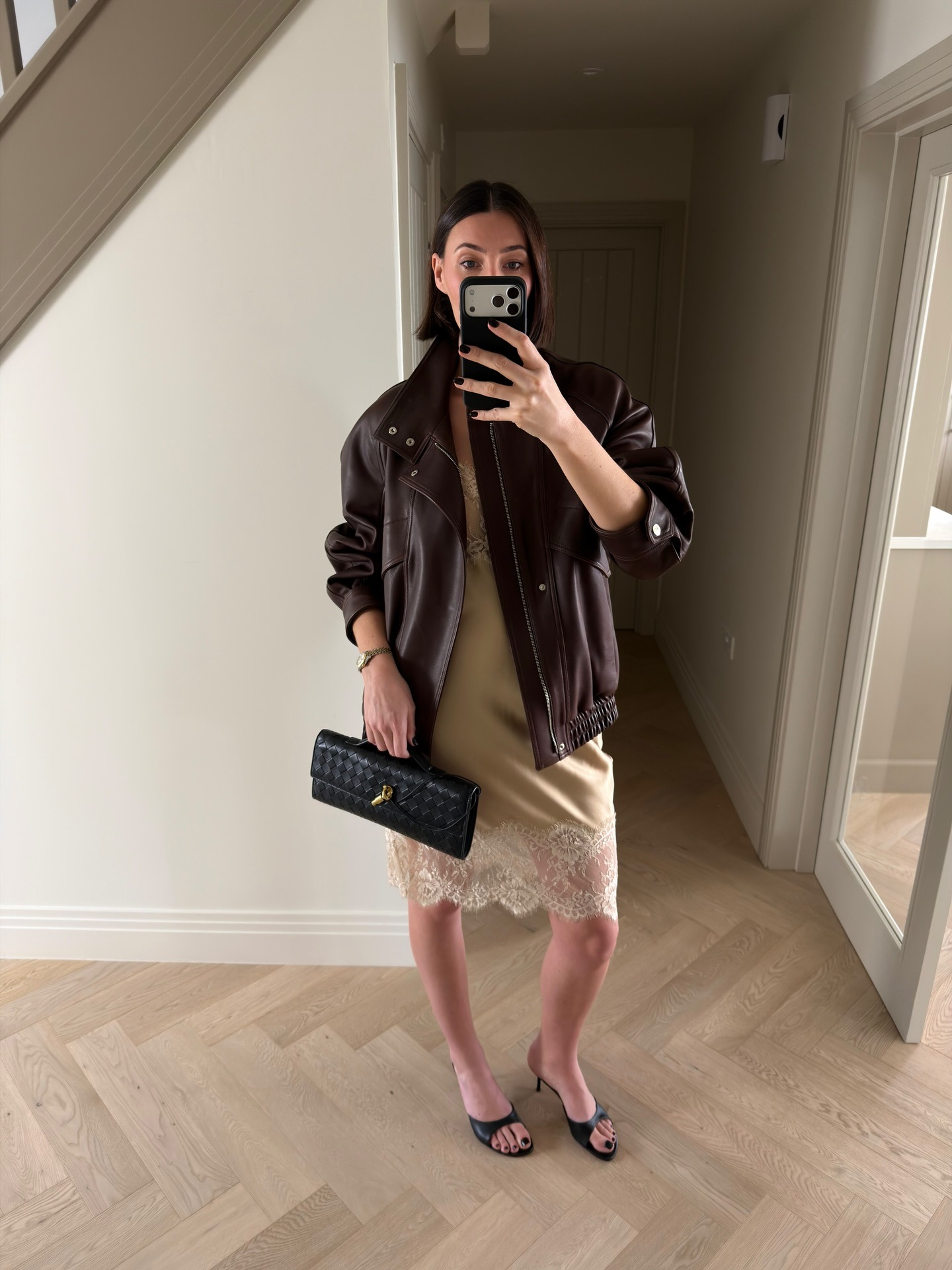 Sarah wears a burgundy leather coat, gold slip dress, black bag, and black heels.