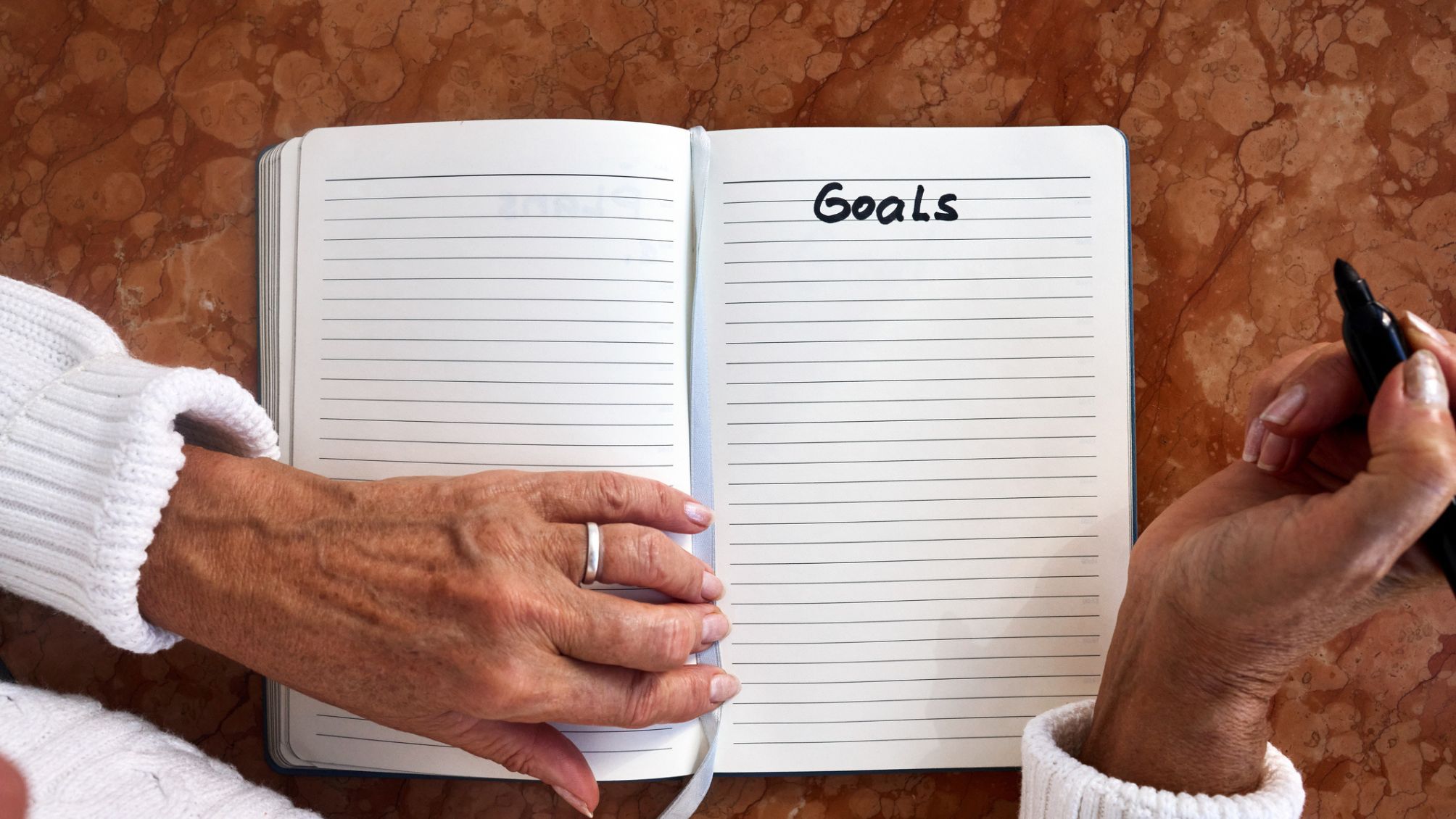 A person writing Goals in a notebook.