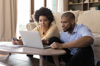 Couple sitting in front of the sofa at home looking at a laptop together